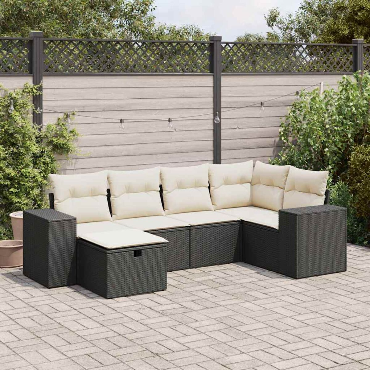 Outdoor-Ecksofa mit cremefarbenen Kissen und dunkelgrauem Korbgeflecht. Auf einer Ziegelterrasse, nahe einem Zaun.