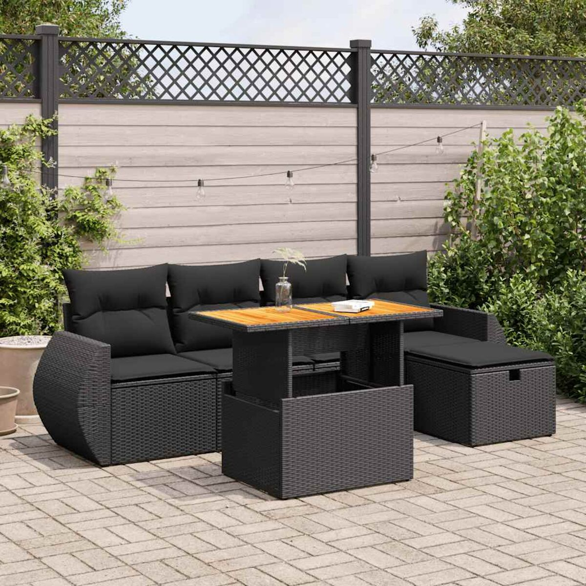 Schwarzes Outdoor-Sofa und Tisch-Set auf einer Terrasse. Im Hintergrund sind Zaun und Grün zu sehen.