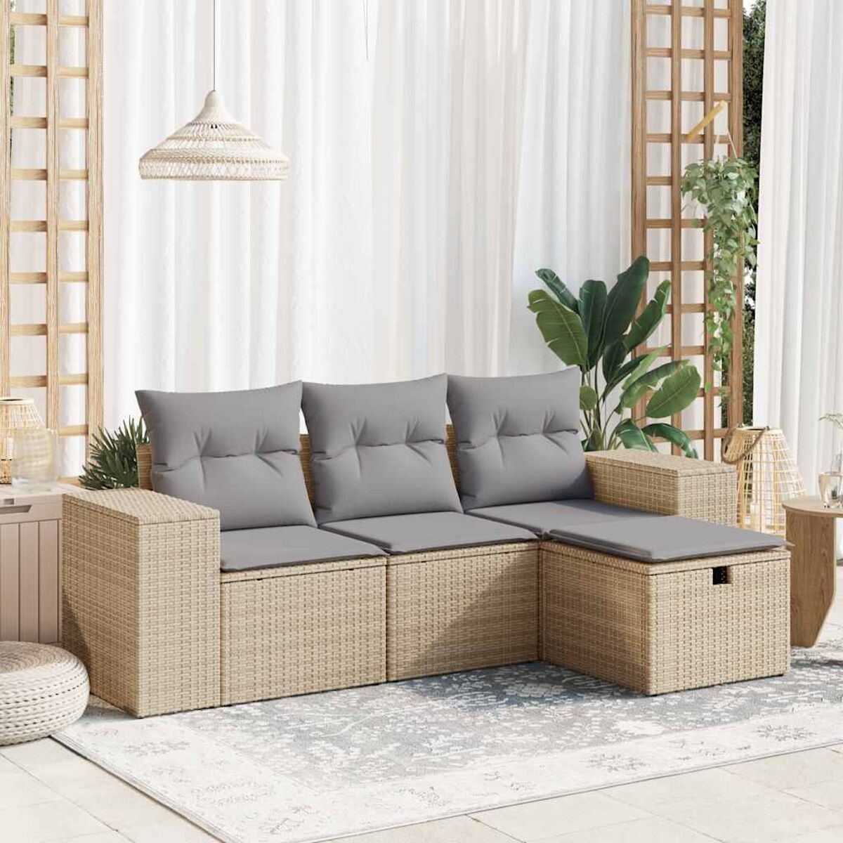 Un divano componibile in rattan con cuscini grigi, un tappeto e piante. Una tenda bianca sullo sfondo.
