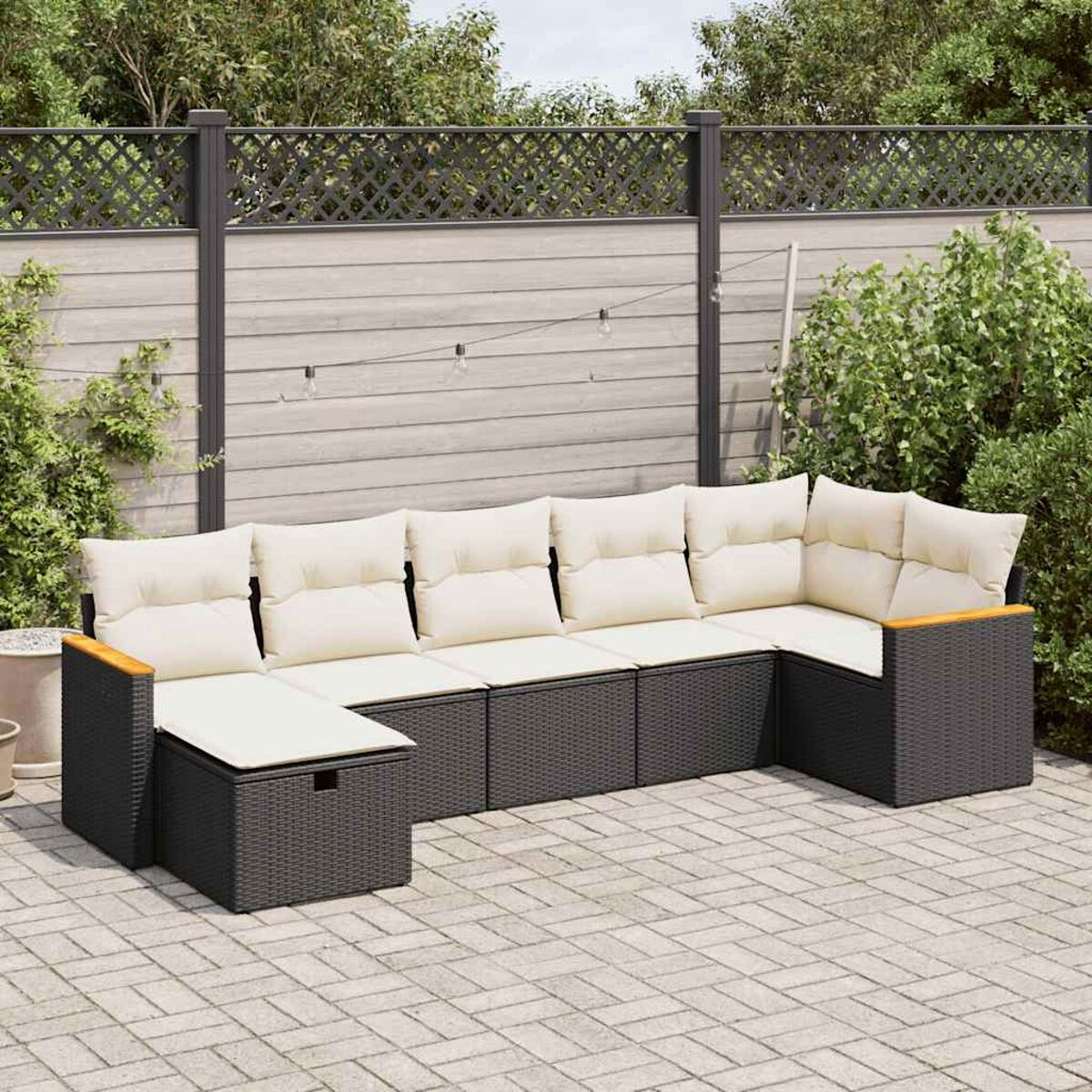 Sofá seccional negro y madera para exteriores en un patio. Fondo: valla y plantas.