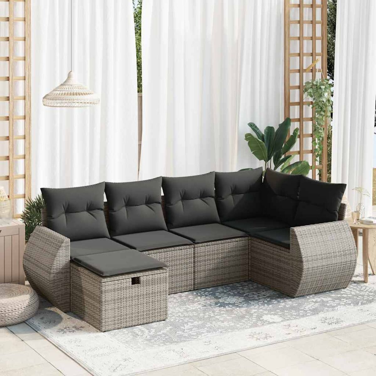 Rattan-Ecksofa mit grauen Kissen auf einer Terrasse. Weiße Vorhänge und Grünpflanzen sind im Hintergrund zu sehen.