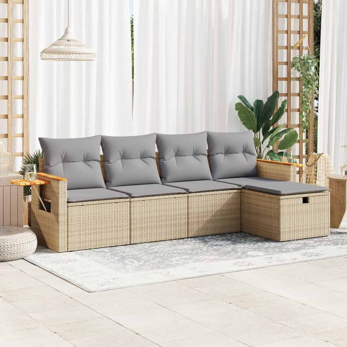Un divano componibile in rattan con cuscini grigi, un tappeto e piante. Una tenda bianca sullo sfondo.