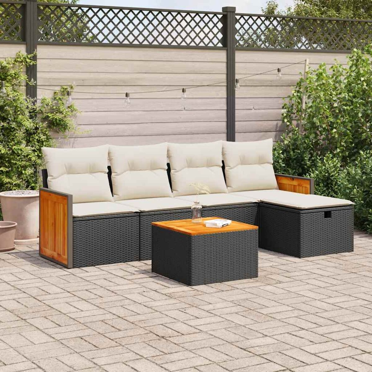 Outdoor-Sitzgruppe auf einer Terrasse. Enthält Sofa, zwei Ottomane und einen Tisch. Natürlicher Hintergrund.