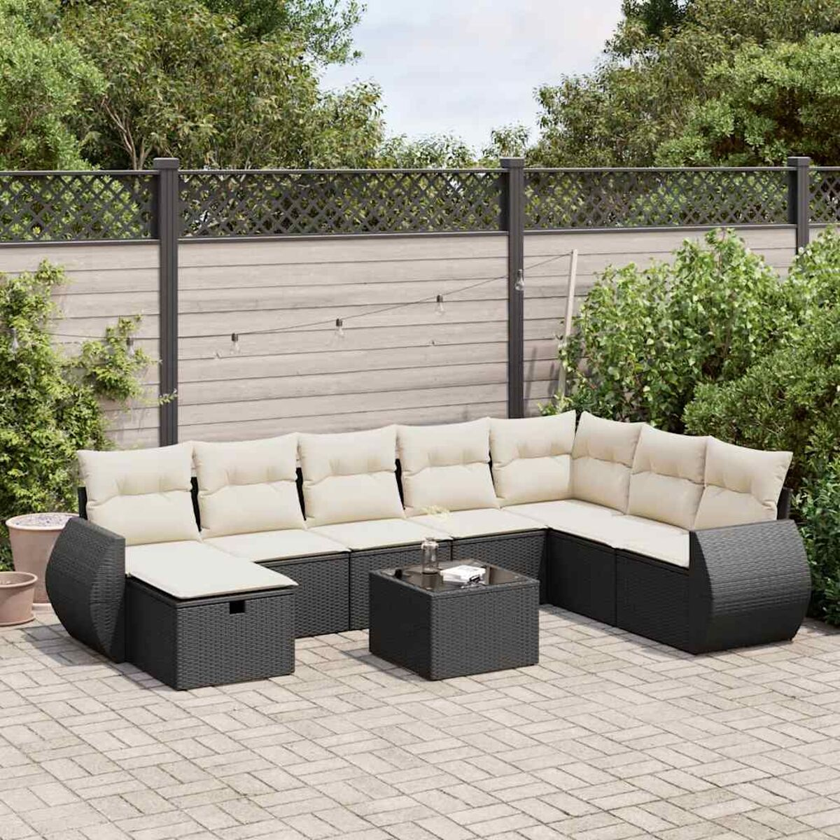 Schwarzes Ecksofa aus Korbgeflecht mit beigefarbenen Kissen auf einer Terrasse. Mit einem schwarzen Tisch.