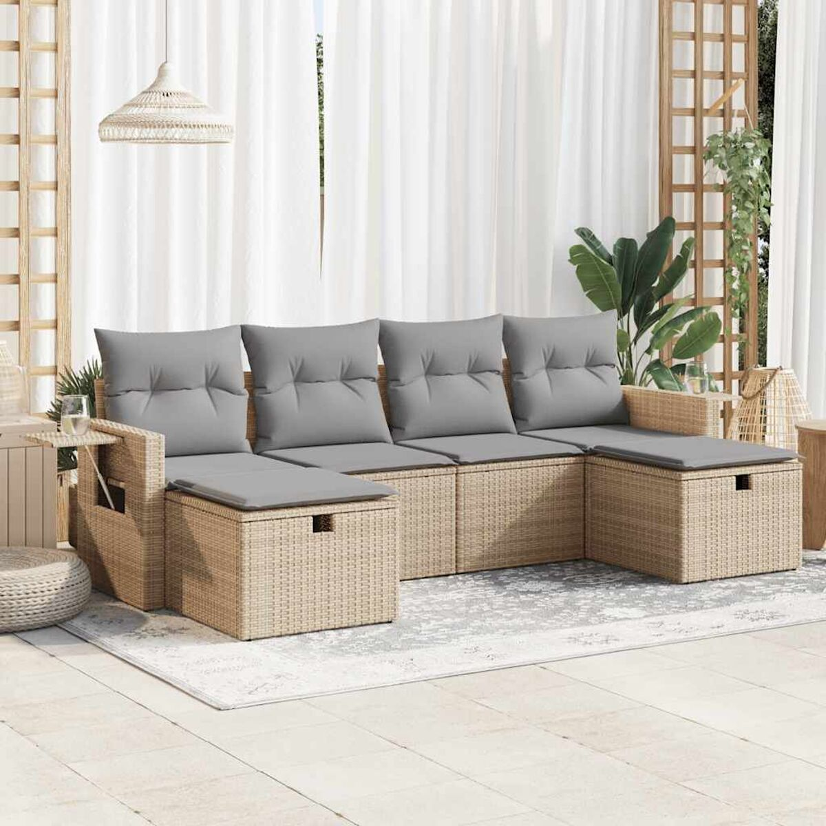 Set divano in vimini beige con cuscini grigi su un patio con tappeto e tende sullo sfondo.