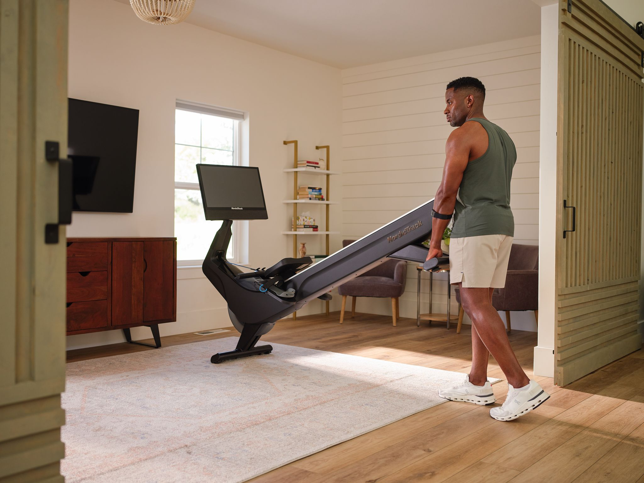 Ein Mann hebt ein Rudergerät in einem Fitnessraum, in der Nähe eines Fernsehers.