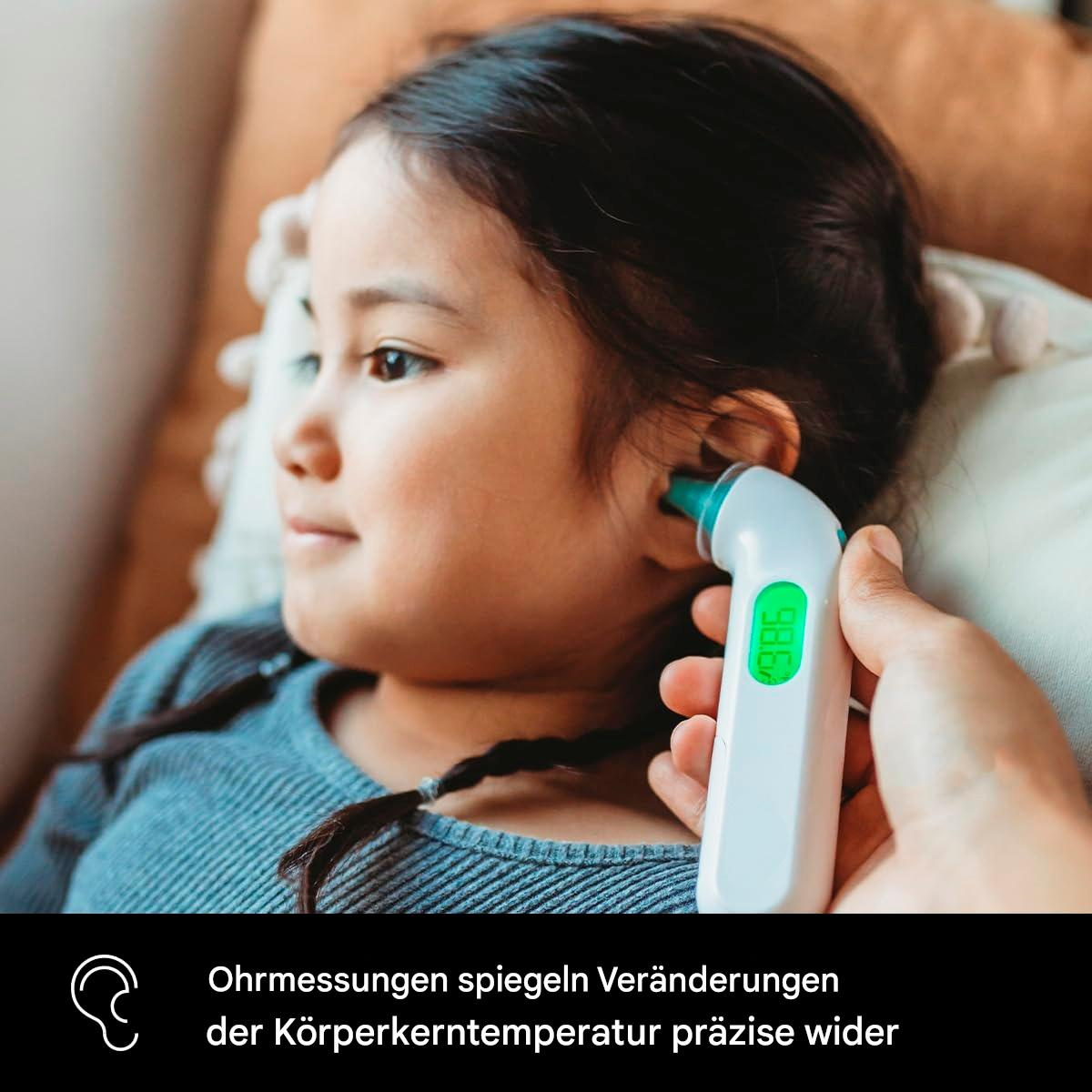Ein Ohr eines Kindes wird mit einem digitalen Thermometer untersucht. Grünes Display zeigt die Temperatur. Kind im Hintergrund.