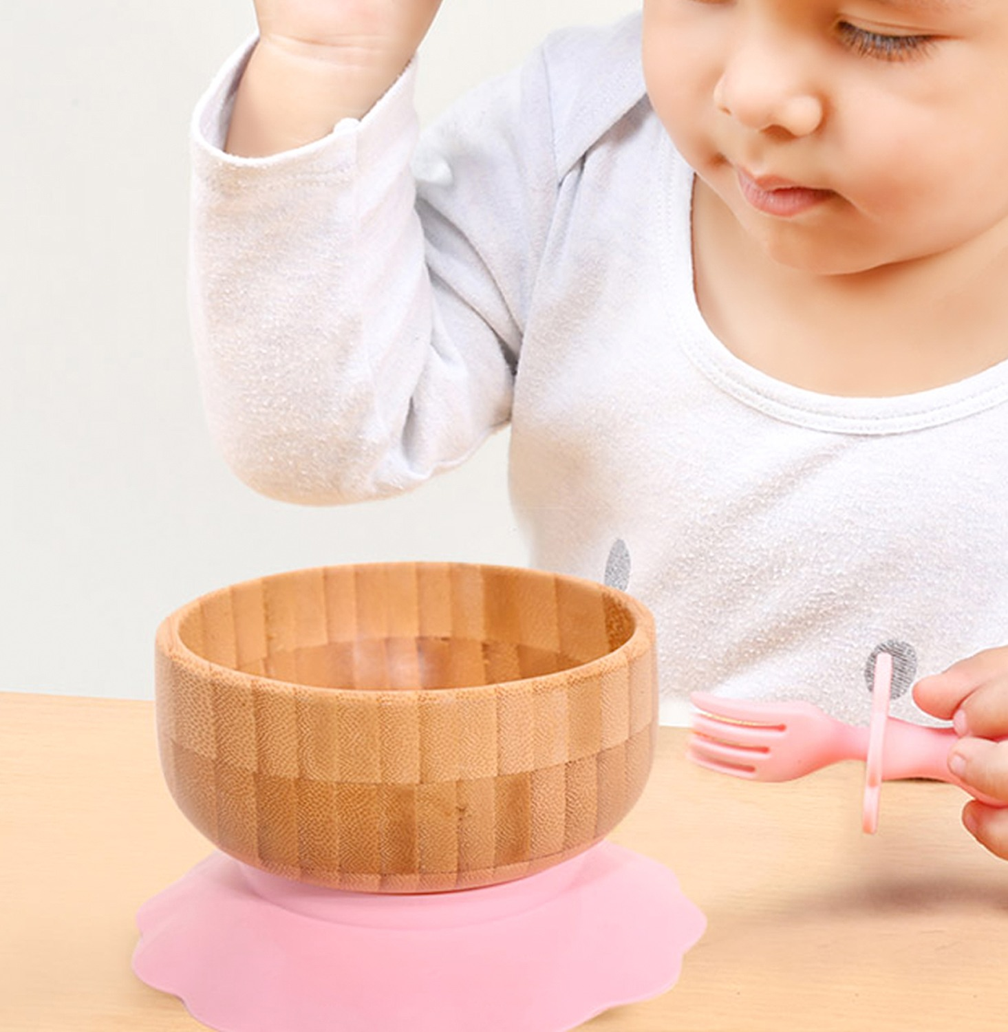 Ein Baby greift nach einer Holzschüssel auf rosa Saugfuß mit einer Gabel.