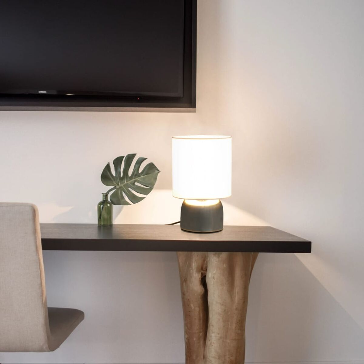 Ein Schreibtisch mit einer Lampe und einer Pflanze. Die Lampe ist an, die Pflanze steht in einer Vase.