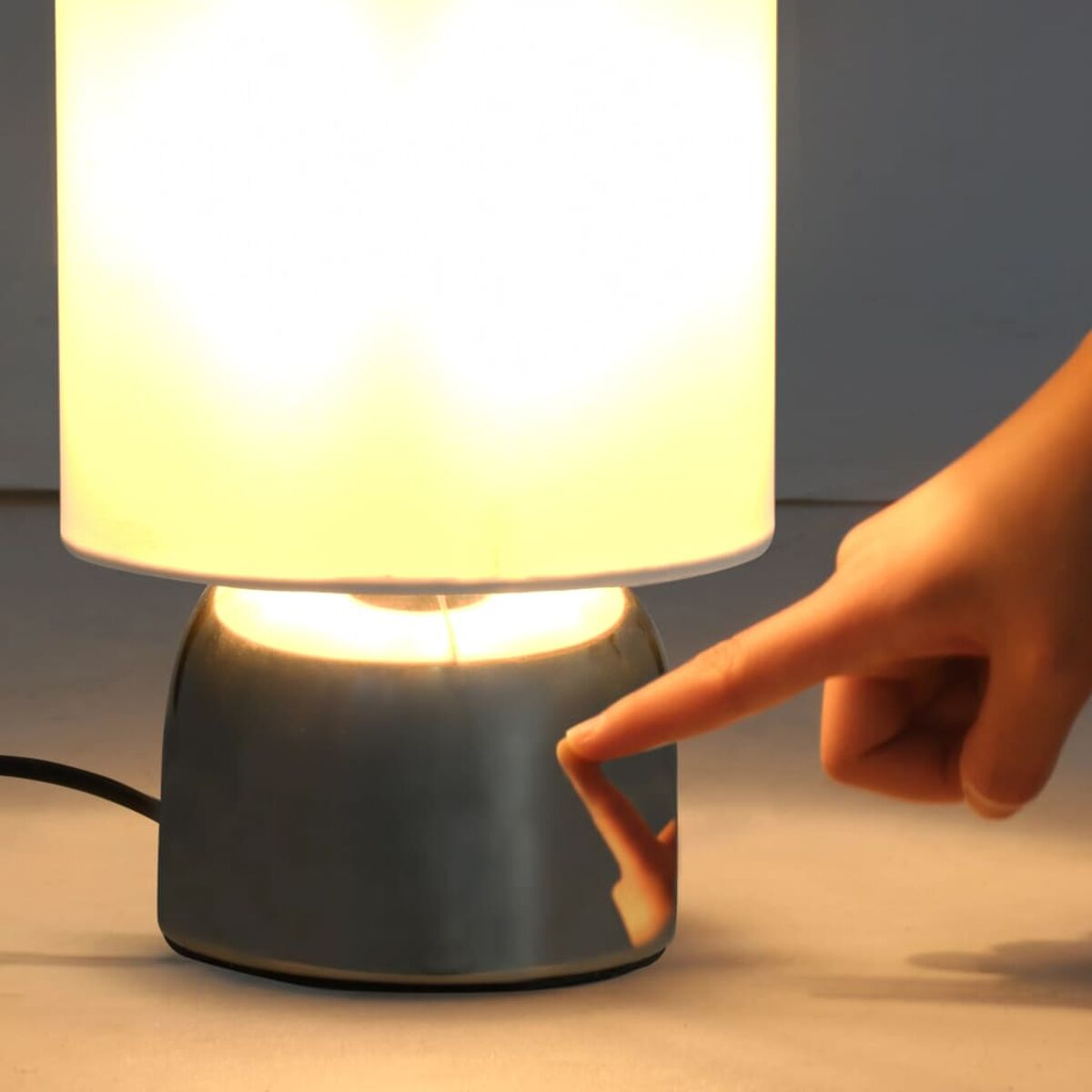 Eine Hand berührt eine silberne Lampe, die Lampe leuchtet.