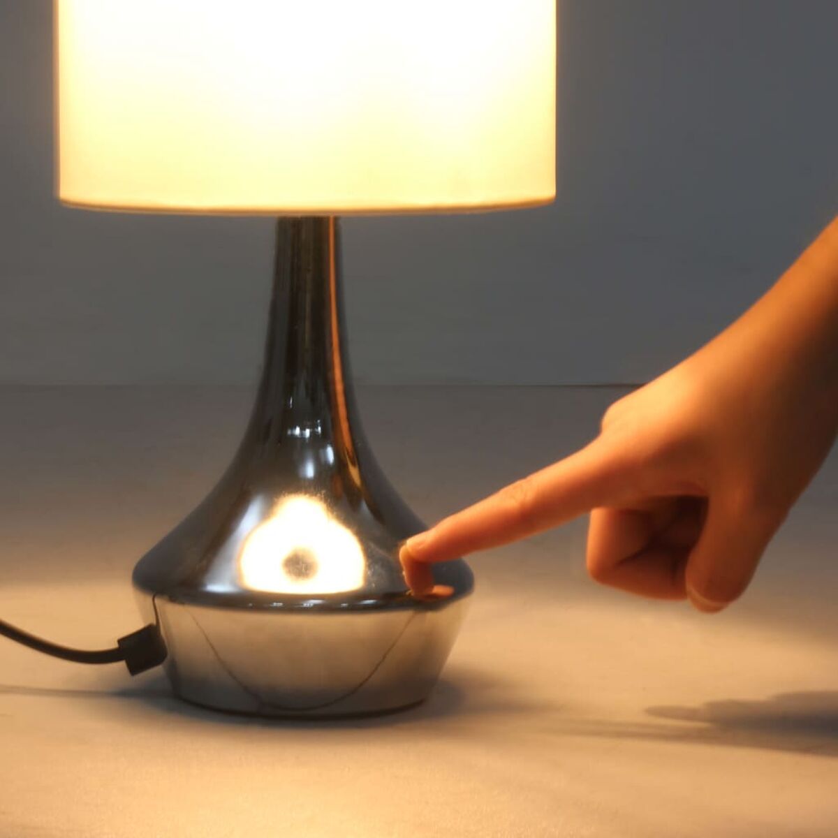 Silberne Lampe mit weißem Schirm, Hand berührt Sockel.