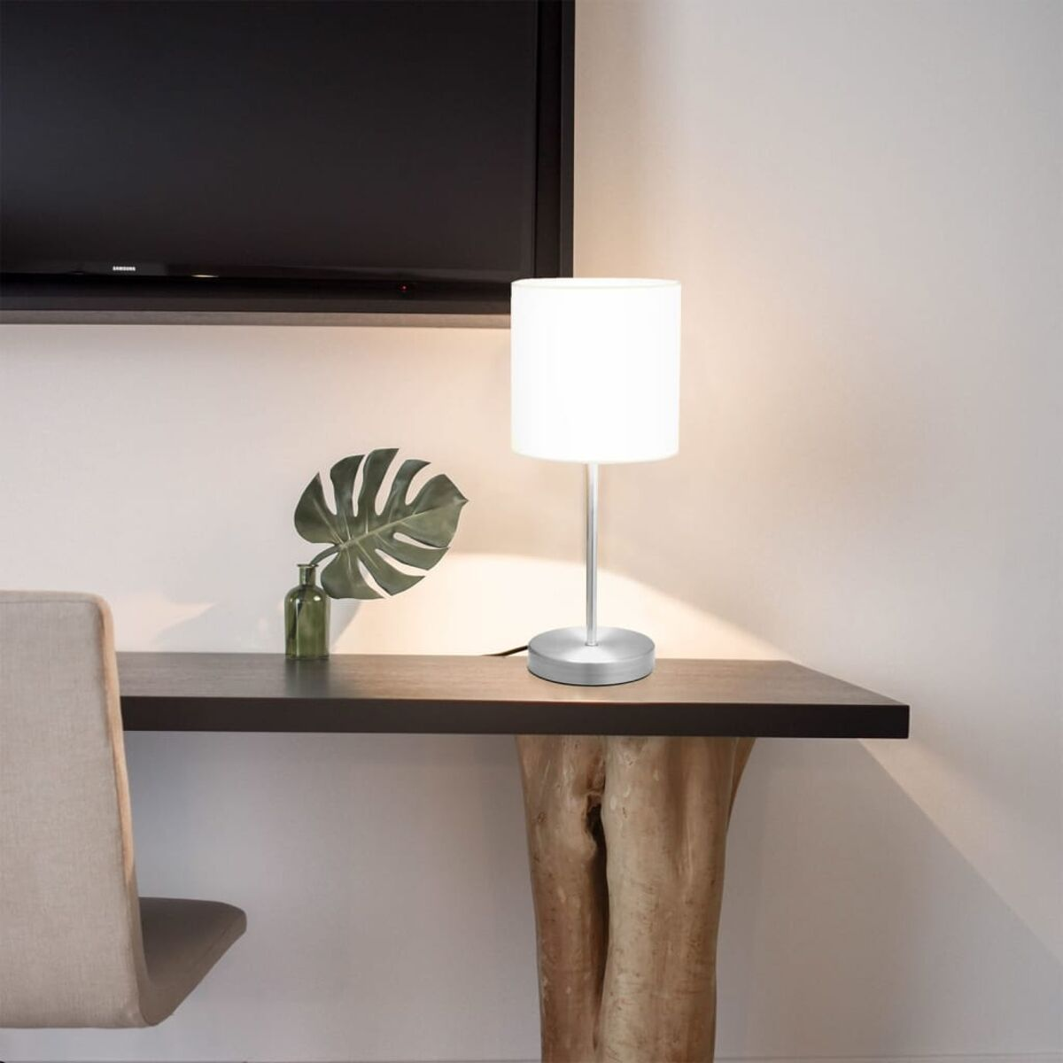 Ein Schreibtisch mit Lampe, Pflanze und Stuhl in einem Raum mit Fernseher.