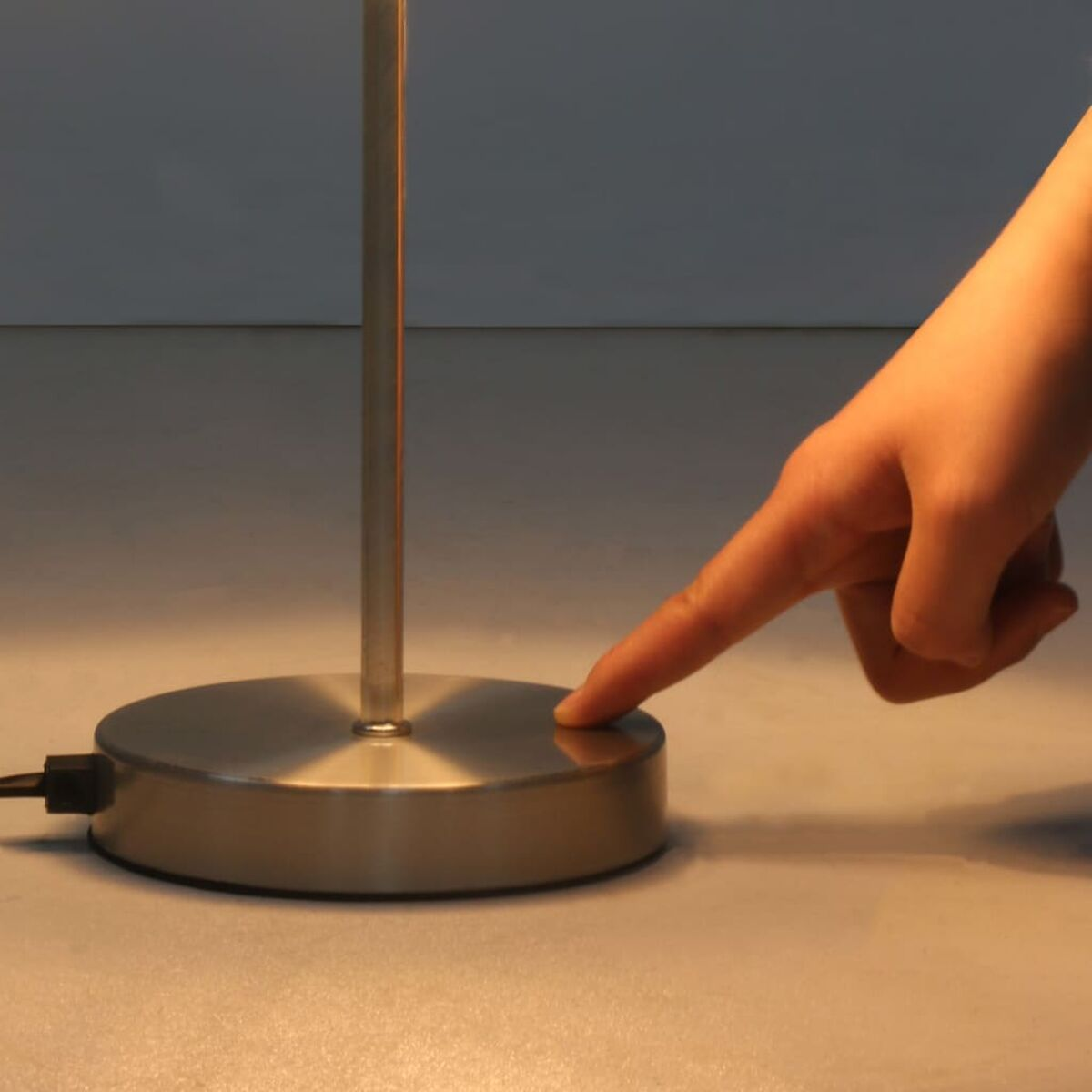 Hand drückt Knopf an einer silbernen Schreibtischlampe.