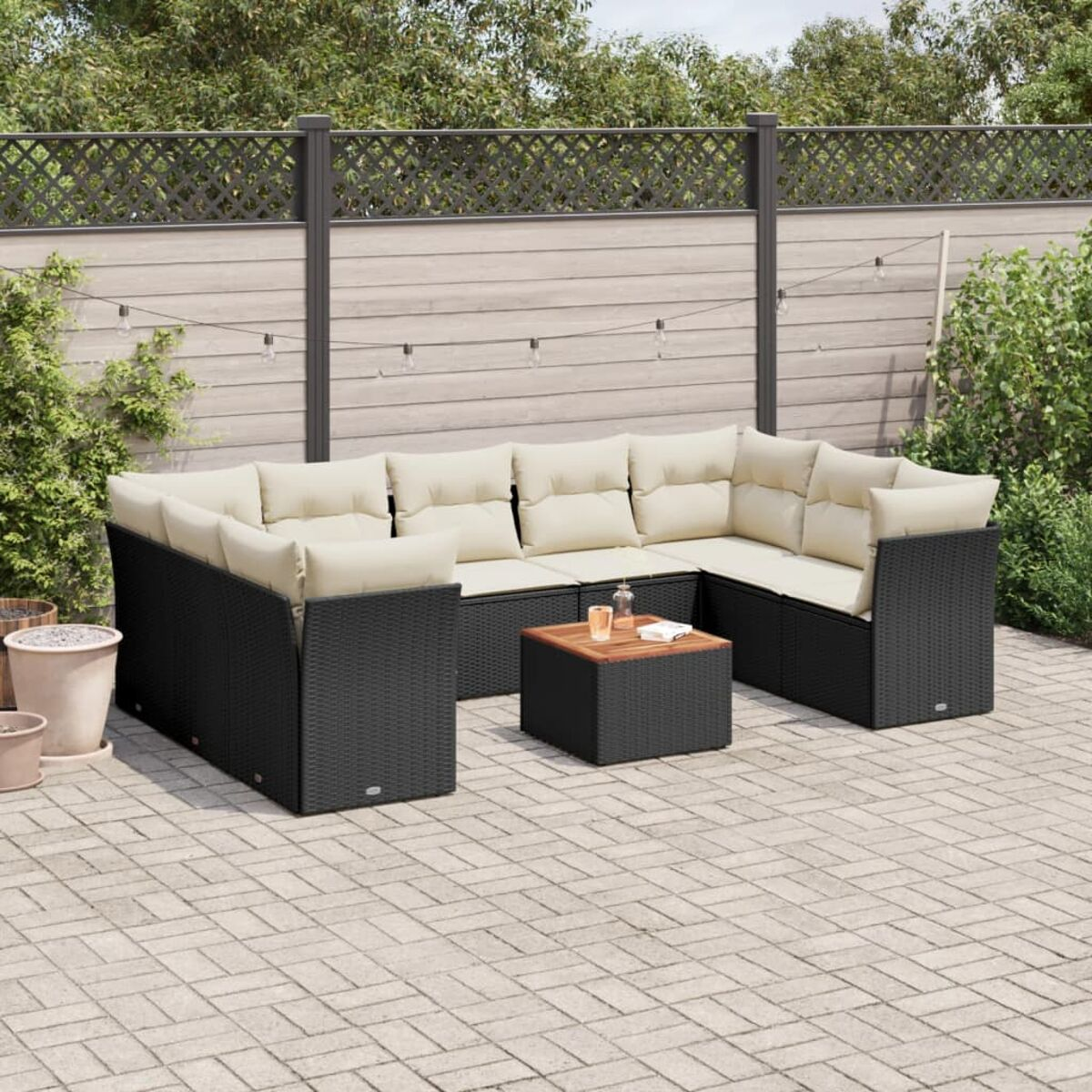 Schwarzes gewebtes Sitzmöbel-Set für den Außenbereich mit cremefarbenen Kissen, Holztisch und Ziegelterrasse.