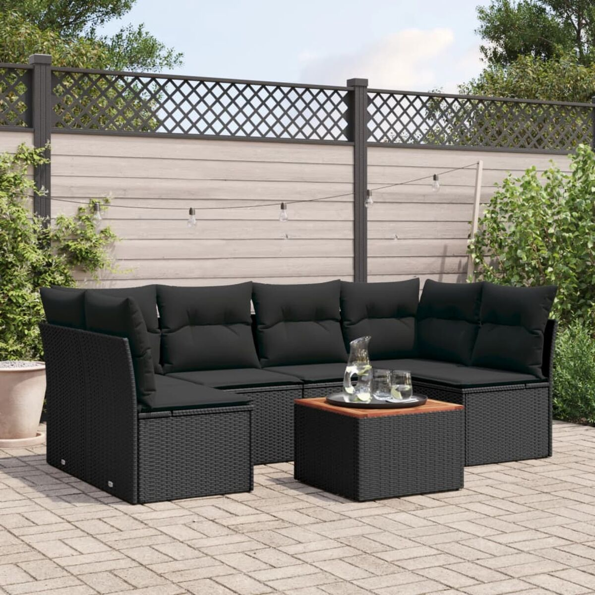 Outdoor-Sofagarnitur aus schwarzem Korbgeflecht mit schwarzen Kissen und einem Couchtisch mit Holzplatte.