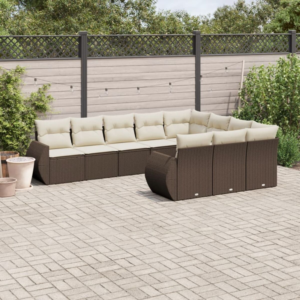 Divano angolare da esterno con cuscini beige. È marrone. Lo sfondo è una recinzione di legno e un patio in mattoni.