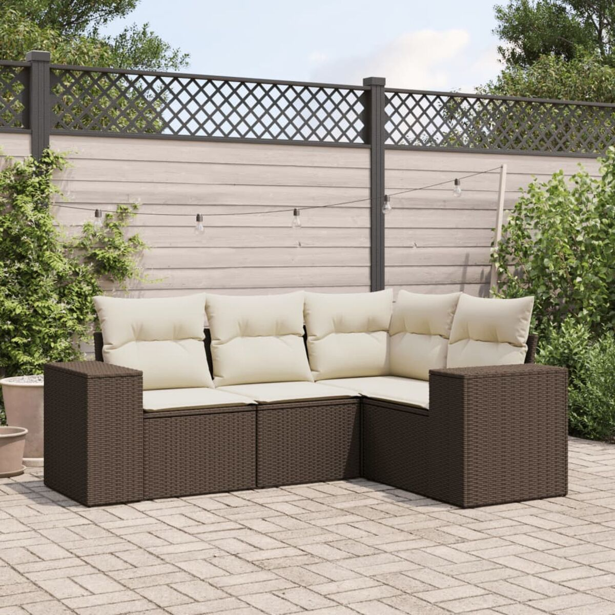 Divano componibile in rattan marrone con cuscini color crema, su un patio. Recinzione in legno sullo sfondo.