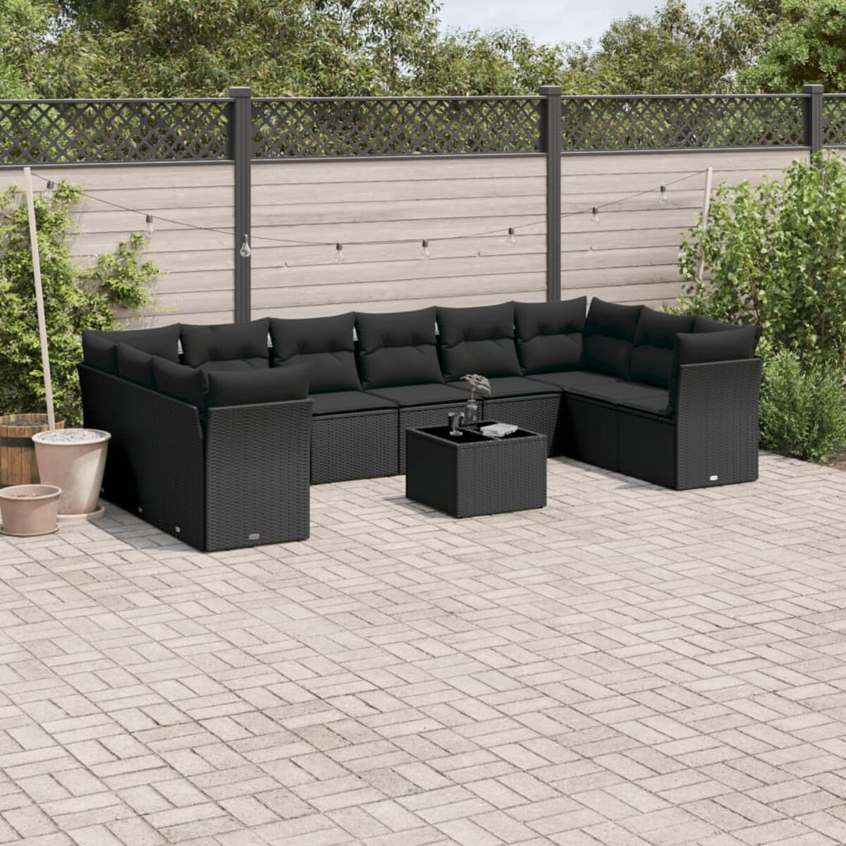 Schwarzes Outdoor-Ecksofa mit schwarzen Kissen und einem kleinen quadratischen Tisch. Die Terrasse ist mit grauen Ziegeln gepflastert.