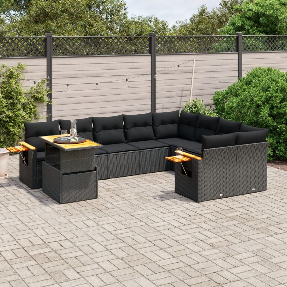 Ein schwarzes Outdoor-Ecksofa mit Tisch und Pool im Hintergrund. Ein Holzzaun.