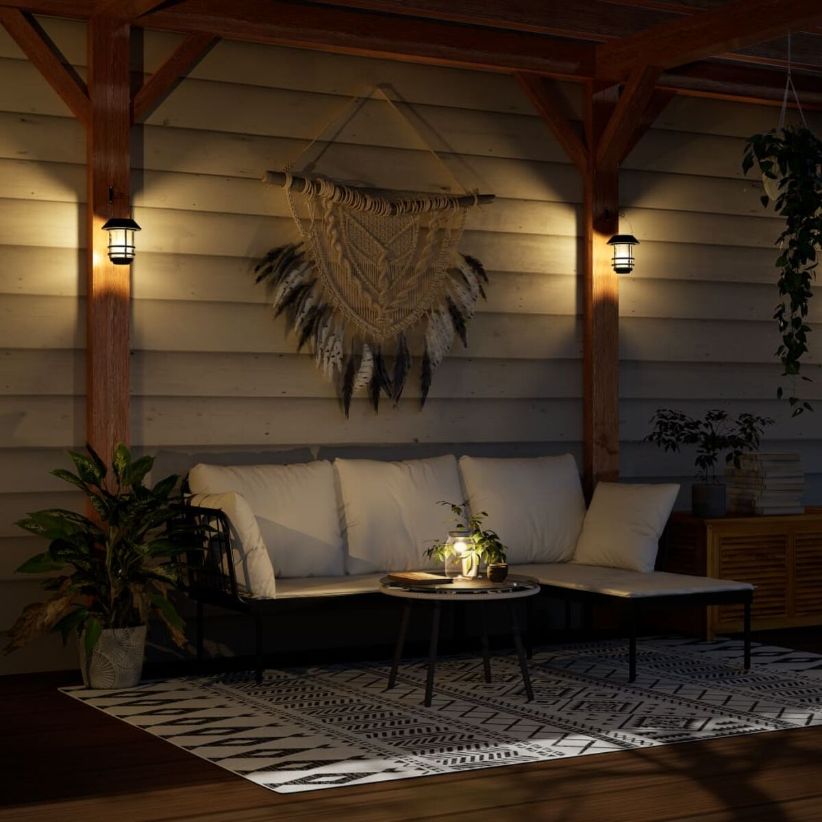 Terrasse mit Sofa, Teppich und Deko. Zwei Lampen an den Holzpfosten. Pflanzen und ein Traumfänger.