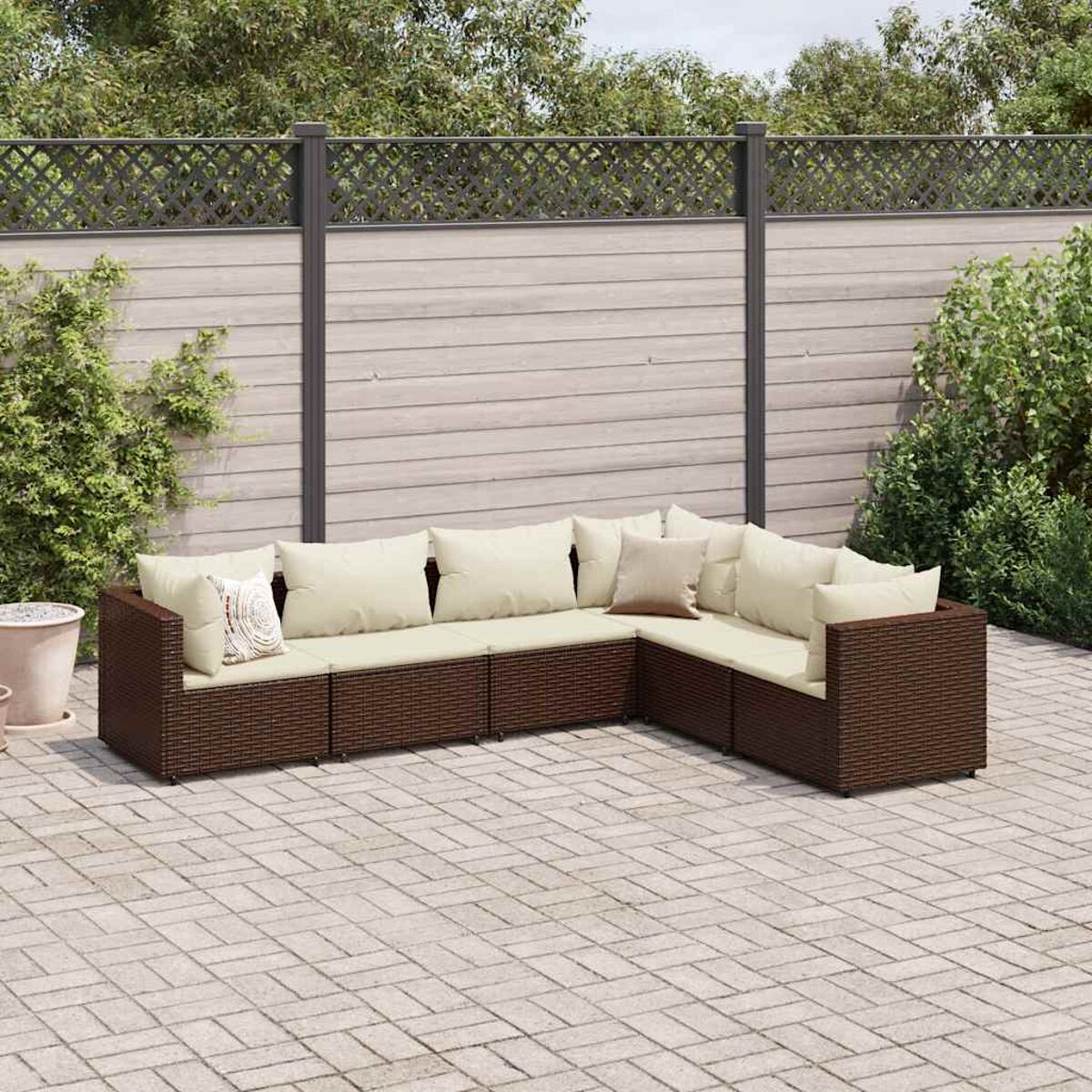 Set di mobili da esterno in vimini marrone su un patio con cuscini beige e piante.