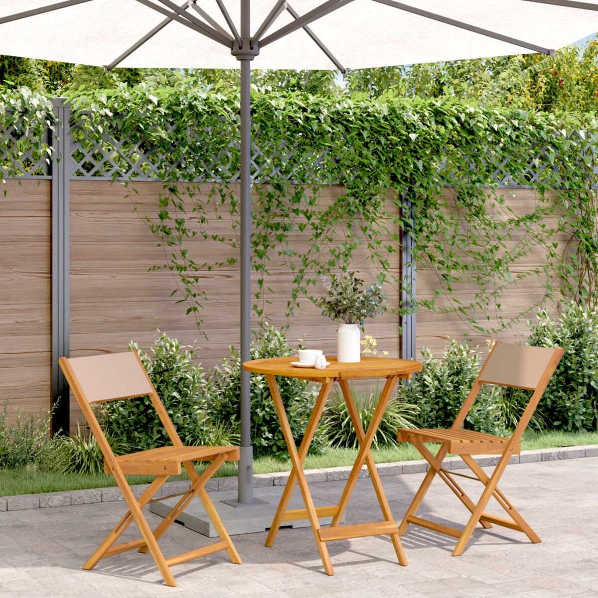 Kleiner runder Tisch, 2 Stühle und ein Sonnenschirm auf einer Terrasse, mit Blumen.