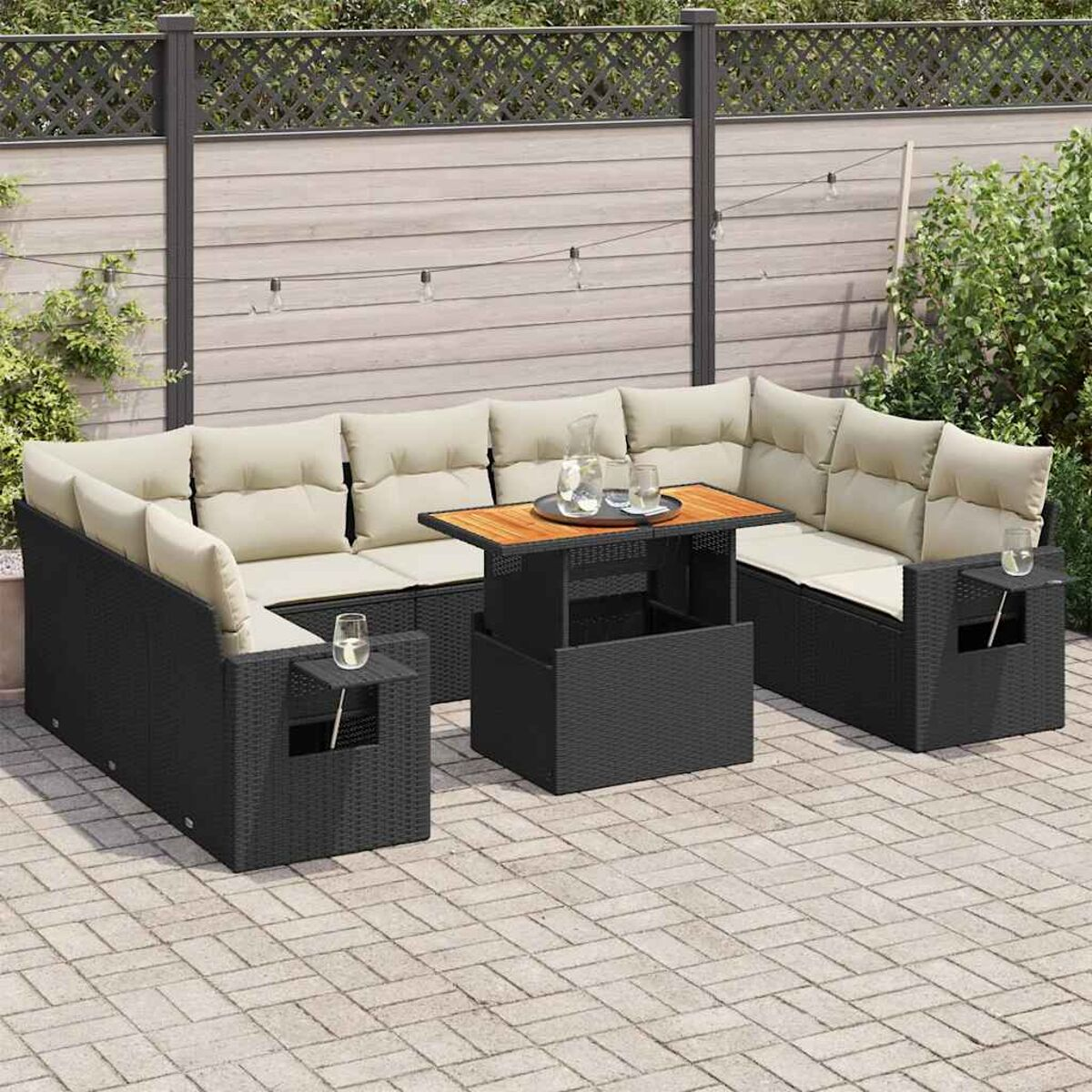 Set divano da esterno in rattan nero con cuscini beige e un tavolino. Accessori visibili.