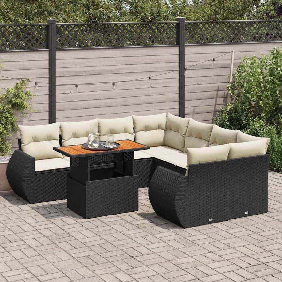 Set di mobili da patio in vimini nero con cuscini beige e un tavolo in legno su un patio in mattoni.