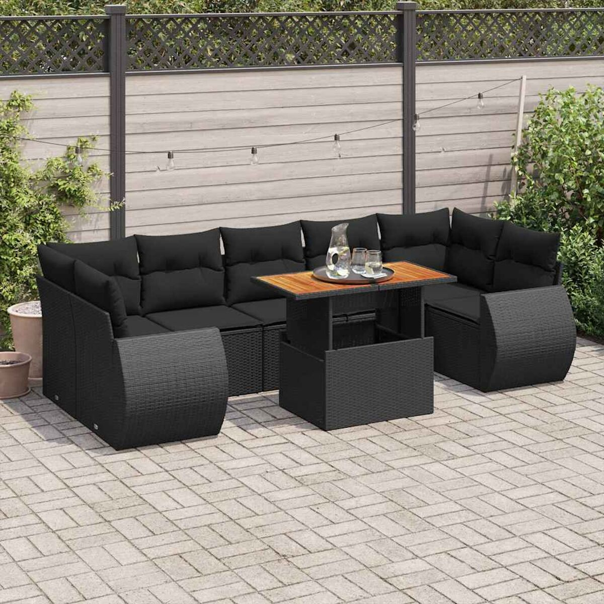 Divano componibile in rattan nero con tavolo, ambiente esterno, cuscini neri e patio pavimentato.