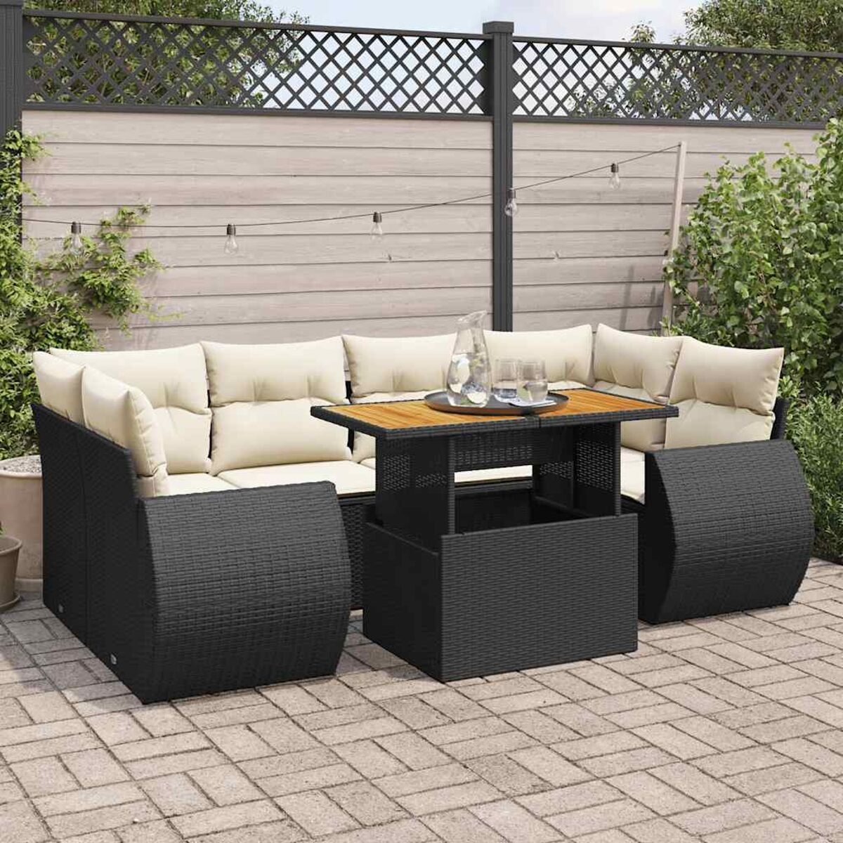 Un set da patio con un divano in vimini nero, un tavolo rialzabile e sedie. Cuscini beige e piante presenti.
