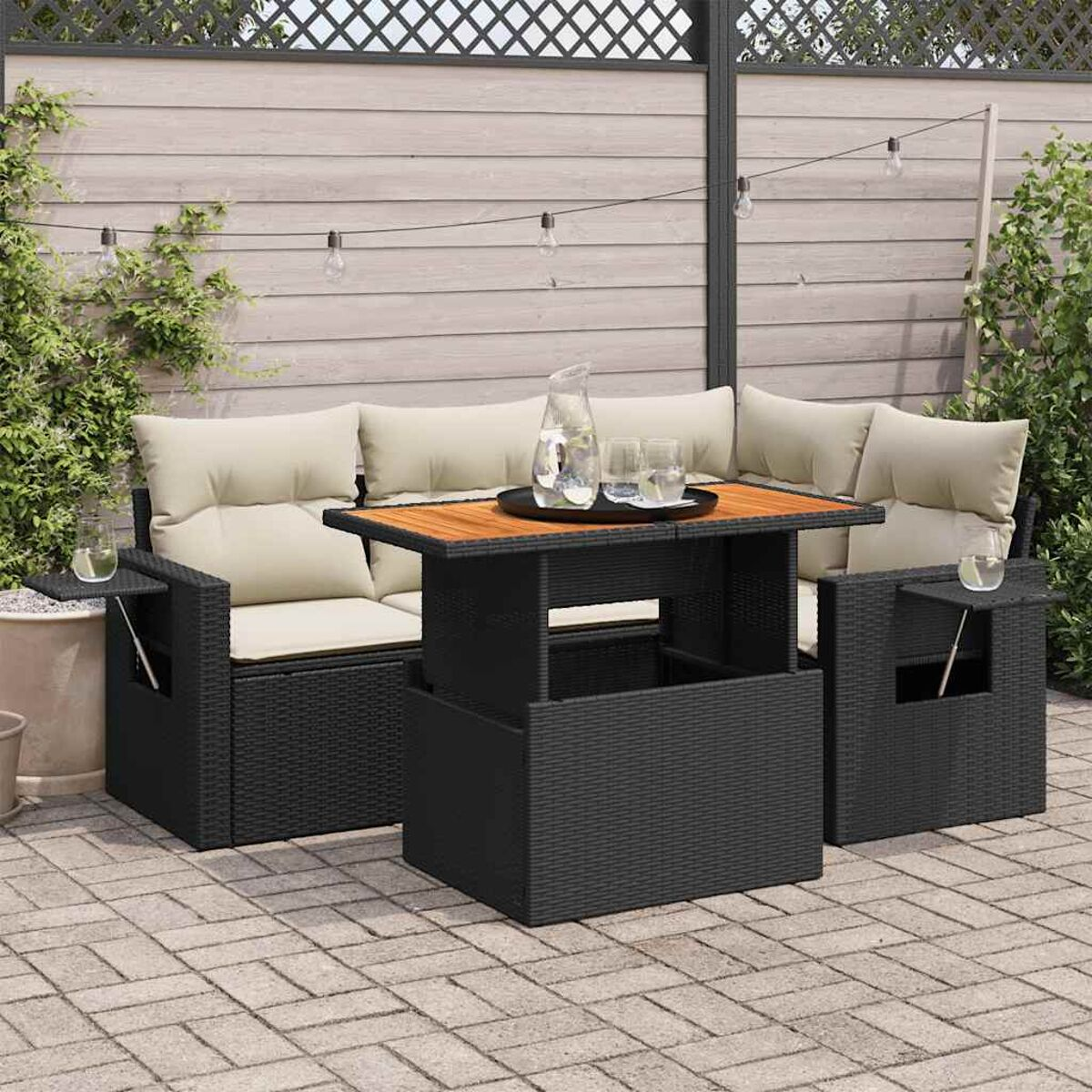 Set patio esterno: divano in vimini nero con due sedie e un tavolo con piano in legno. Cuscini beige e pavimentazione.