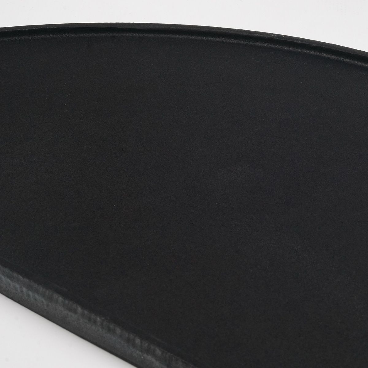 Black, round griddle pan. The surface has a dark, matte finish. The edges have a slight curve.