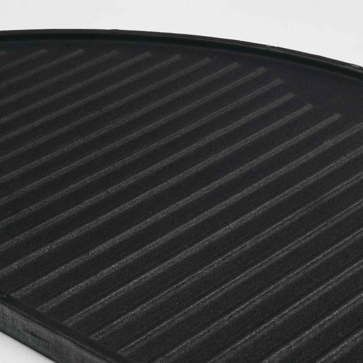 Close-up of a black, curved, ridged cast iron griddle pan. The ridges are in parallel lines.