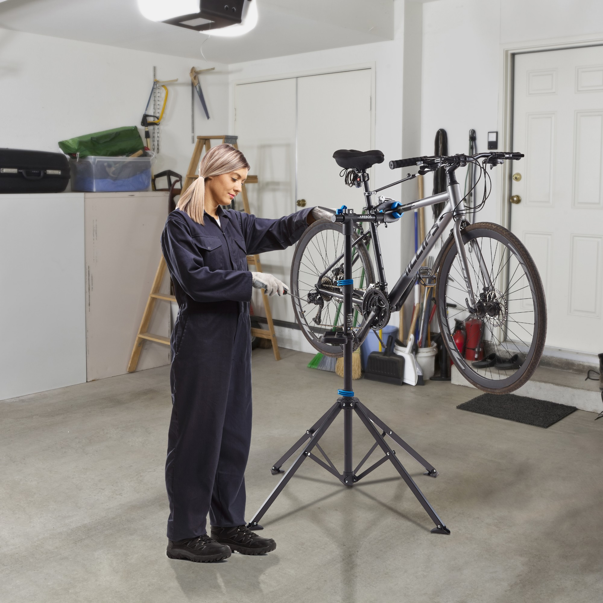 Frau repariert Fahrrad auf einem Ständer in einer Garage. Werkzeuge und Ausrüstung sichtbar.