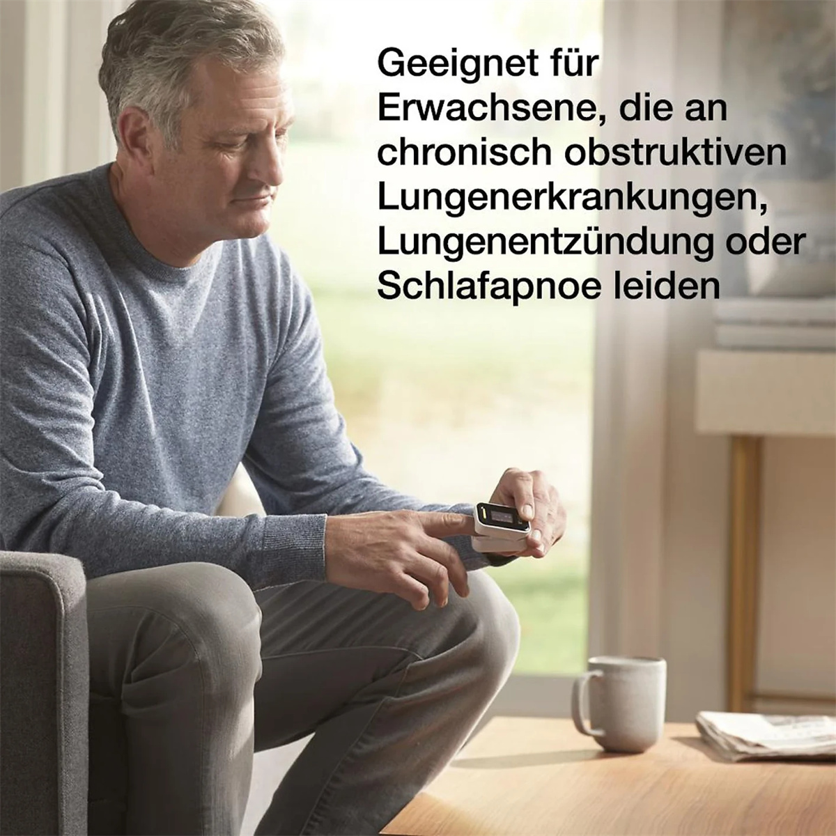 Mann sitzt und hält ein Gerät am Finger. Text in Deutsch vorhanden.
