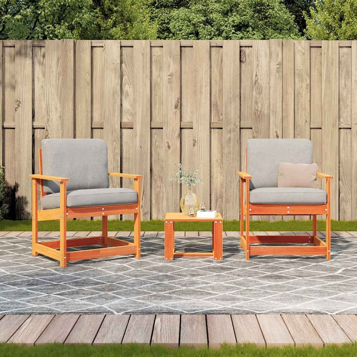 Sedie in legno da esterno con cuscini grigi e un tavolino quadrato. Il set è su un patio in pietra con vegetazione.
