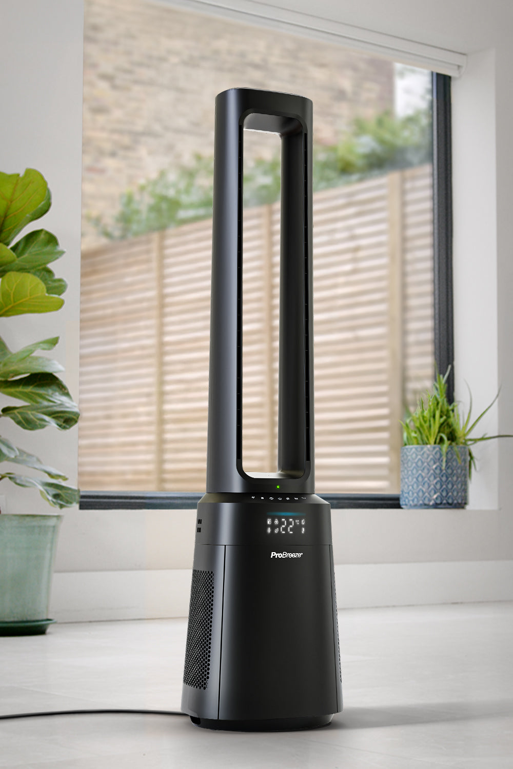 Schwarzer Turmventilator neben einem Fenster. Grün und ein Display sichtbar.