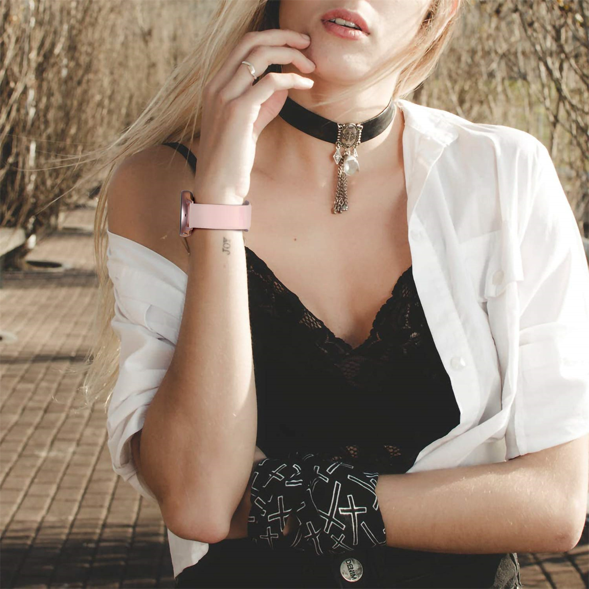 Eine Frau mit schwarzem Halsband und rosa Uhr, mit weißem Hemd und schwarzem Oberteil.