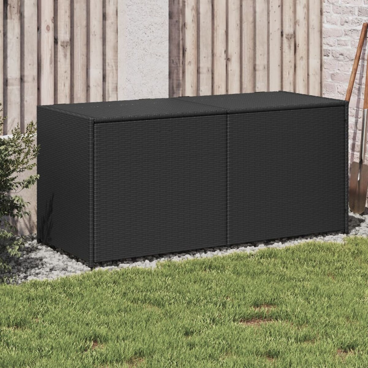 Schwarze Korb-Aufbewahrungsbox auf Gras mit hölzernem Zaun im Hintergrund und einer Schaufel.