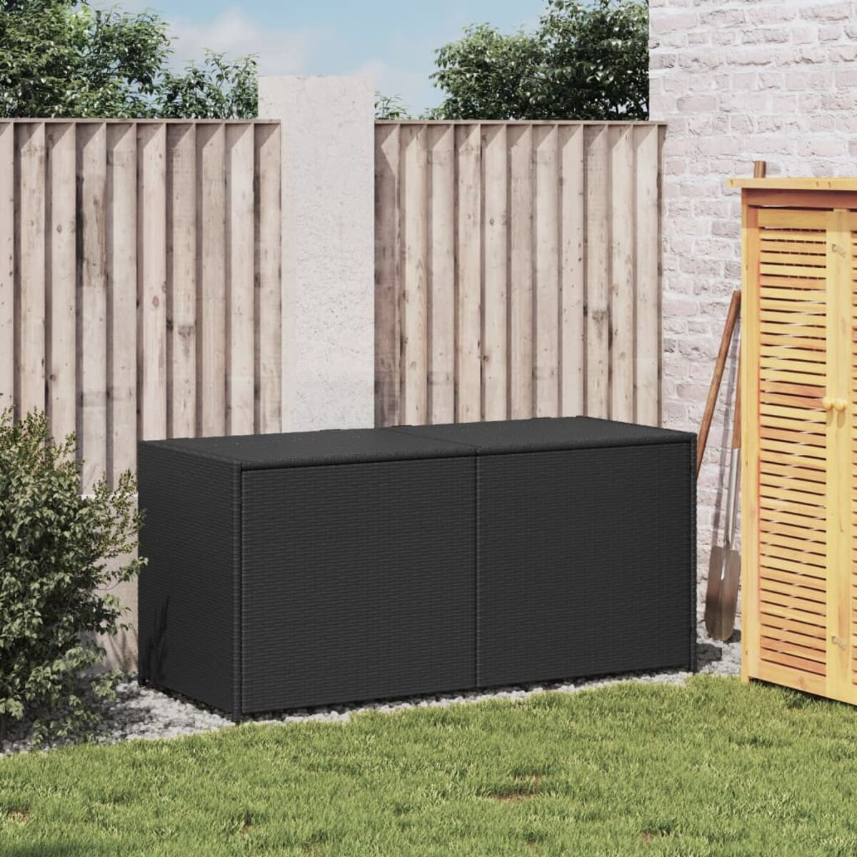 Eine schwarze Aufbewahrungsbox im Garten. Sie befindet sich in der Nähe eines Holzzauns und eines Schuppens.