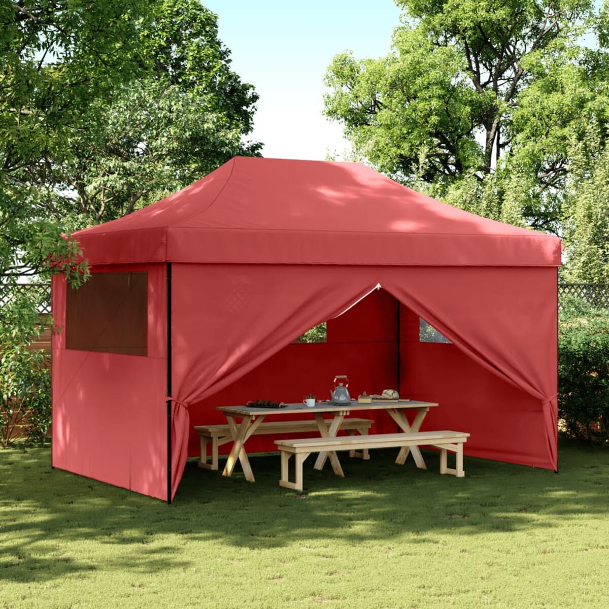 Rotes Zelt mit Picknicktisch, Bänken und Bäumen im Hintergrund auf grünem Gras.