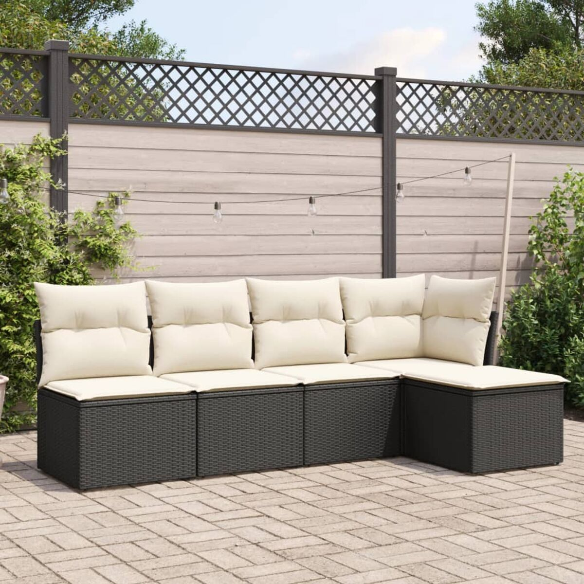 Dunkelgraues Korbsessel-Sofa mit cremefarbenen Kissen auf gepflasterter Terrasse.