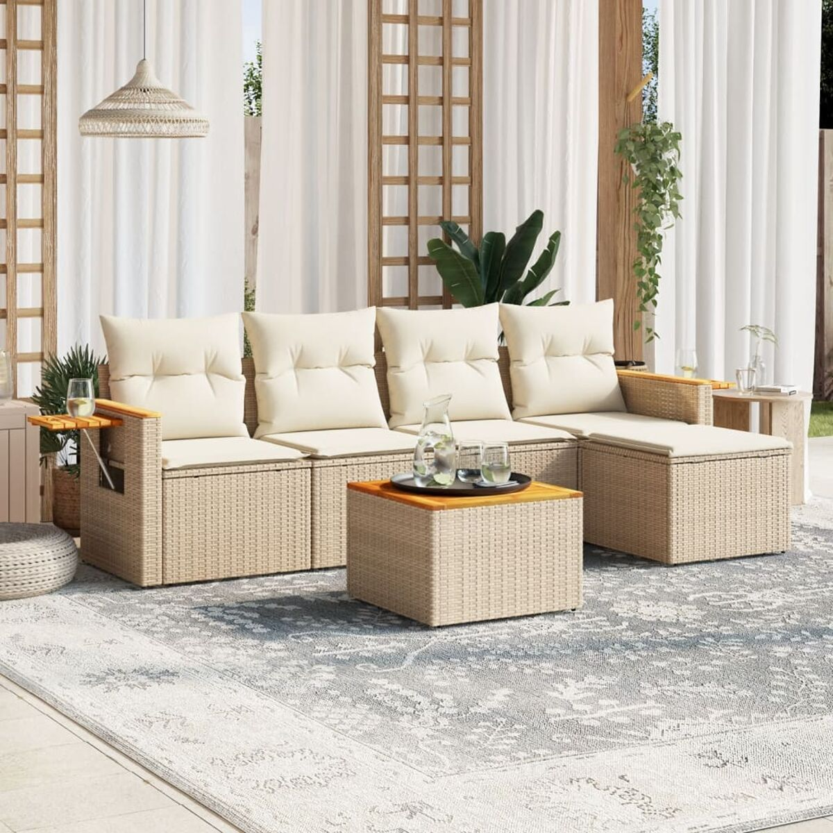 Gartenmöbel-Set aus Korbgeflecht mit Kissen, Tisch und Teppich. Durchscheinende Vorhänge und Pflanzen sichtbar.