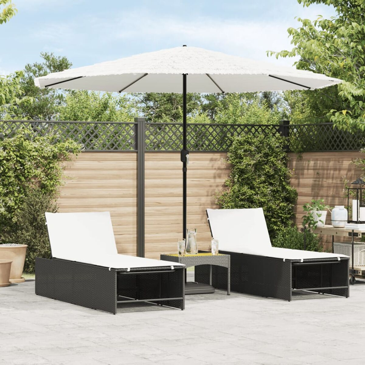 Zwei schwarze Liegestühle aus Korbgeflecht, ein kleiner Tisch und ein weißer Sonnenschirm im Garten.