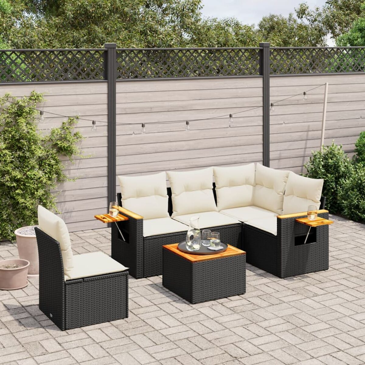 Terrassenmöbel-Set mit Rattanmöbeln: Sofa, Stuhl, Tisch, cremefarbene Kissen und gepflasterte Terrasse.