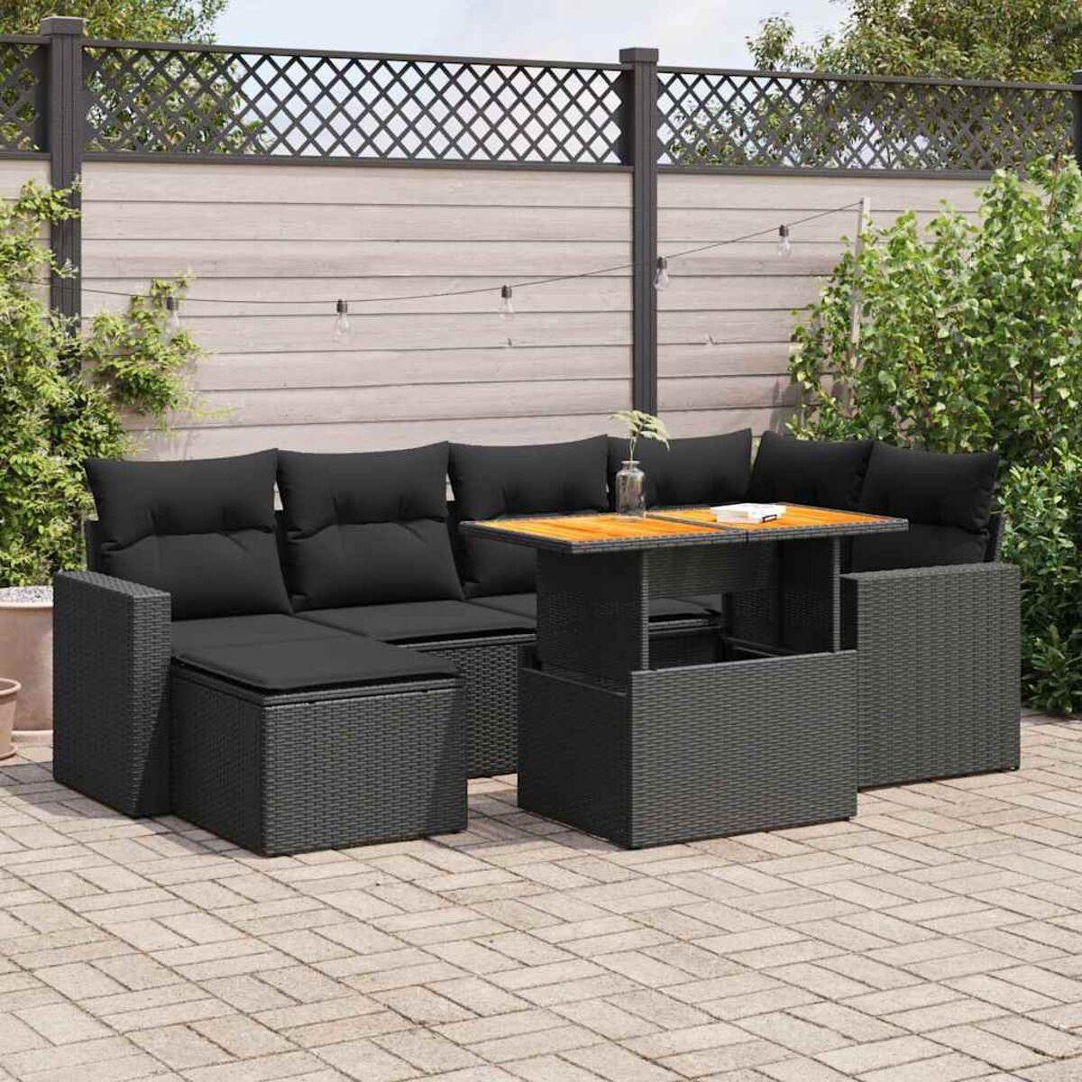 Set di mobili da esterno in vimini nero con tavolo e cuscini neri. Lo sfondo è un patio.