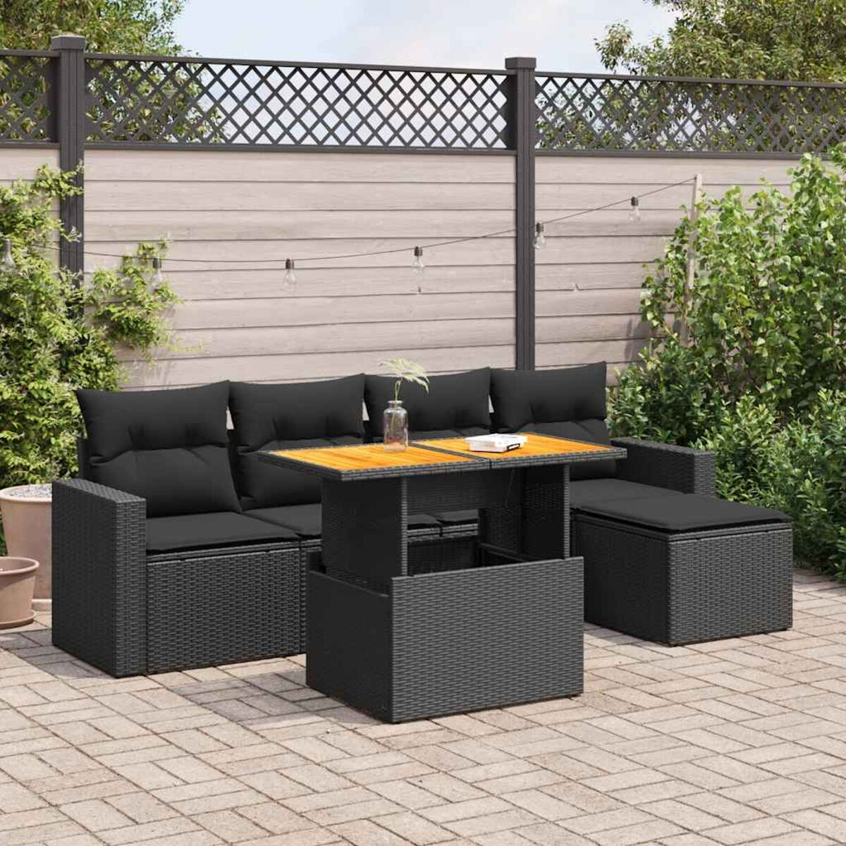 Set da patio esterno con cuscini neri e un tavolo. Lo sfondo include una recinzione e vegetazione.