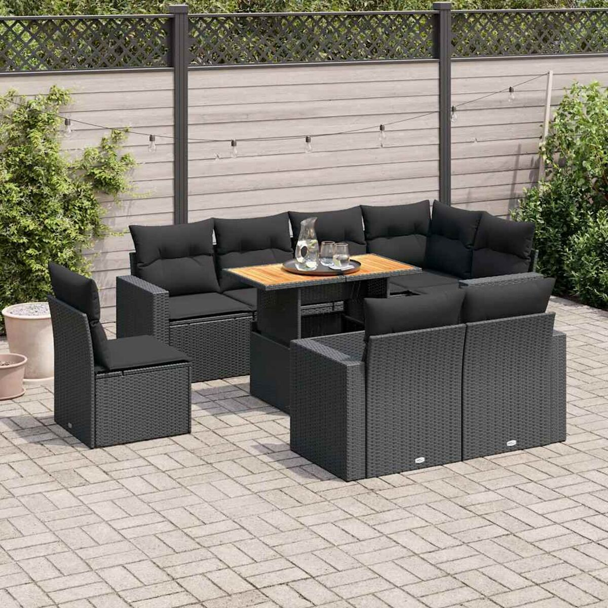 Un set da patio con cuscini neri, tra cui un divano, sedie e un tavolo. Mobili in vimini grigi.