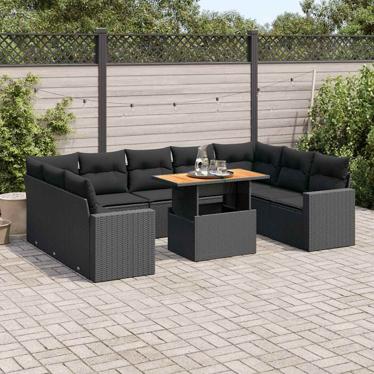Set di sedute da esterno con cuscini neri e un tavolo su un patio pavimentato.
