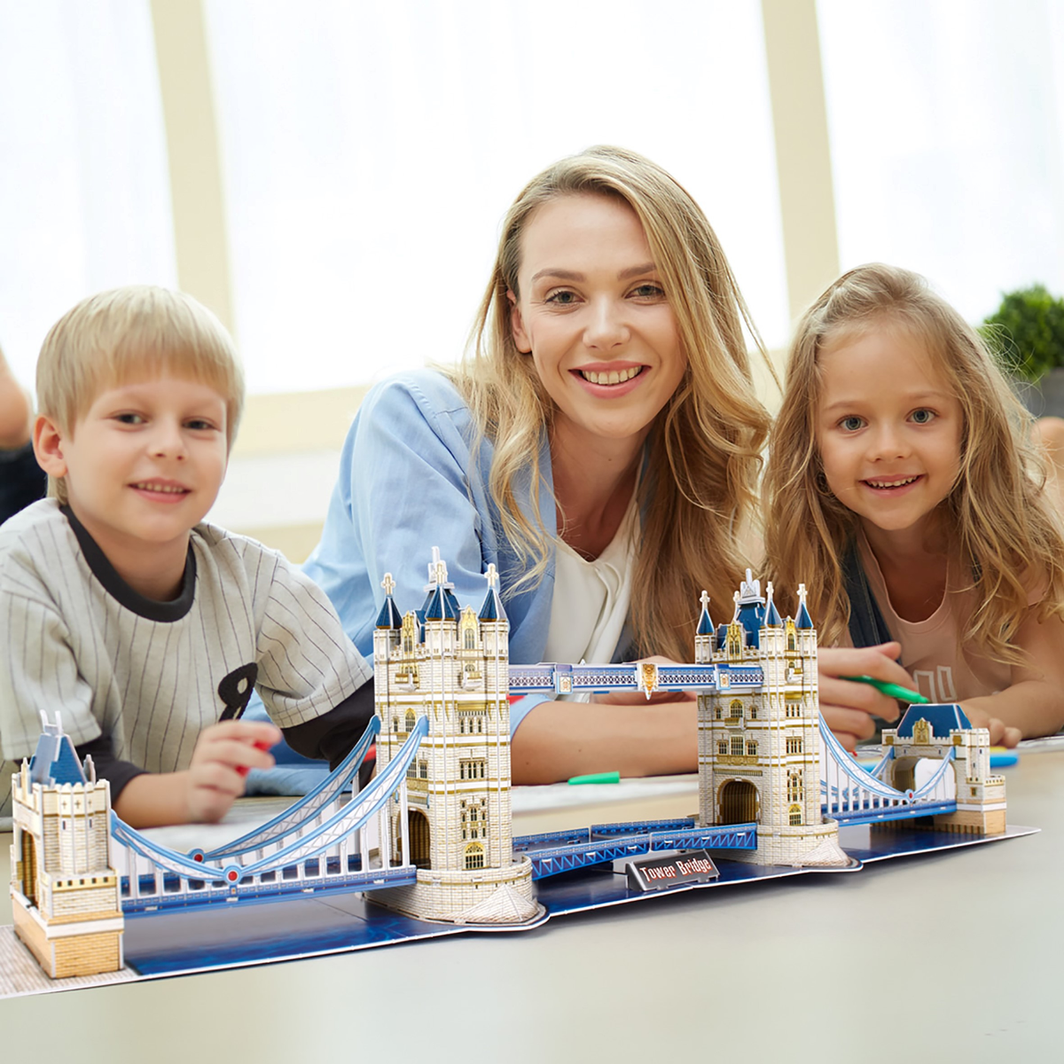 Family smiles with a Tower Bridge model. Foreground: model. Background: window.